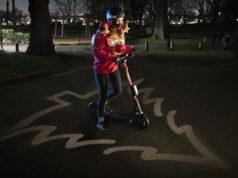 Una sudadera que dibuja 1,5 metros de seguridad alrededor de ciclistas Mujer en patinete con luces navideñas.