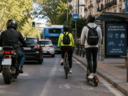 Motorista, ciclista y usuario de patinete circulando en entorno urbano con tráfico y elementos de protección