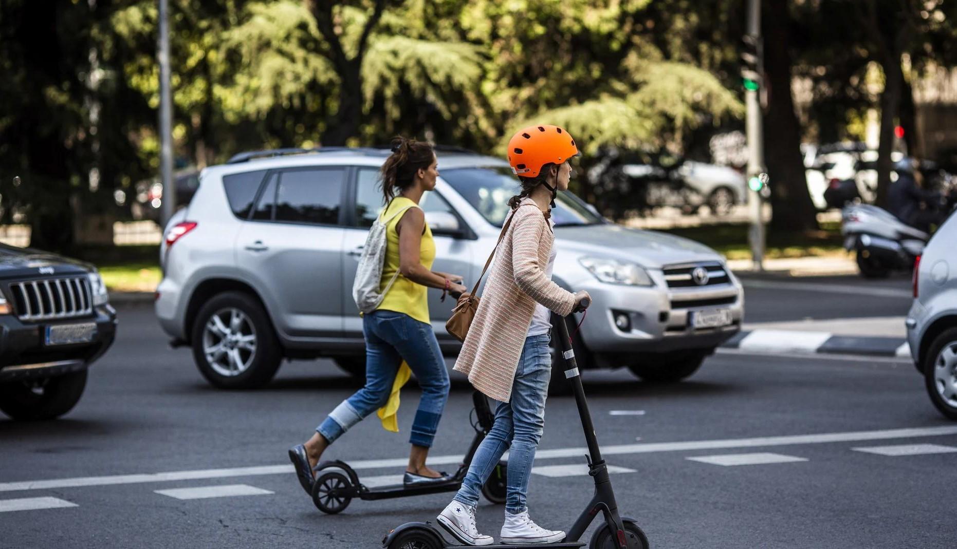 Usuario de patinete eléctrico circulando por una vía urbana habilitada, con casco y respetando el espacio de los peatones.