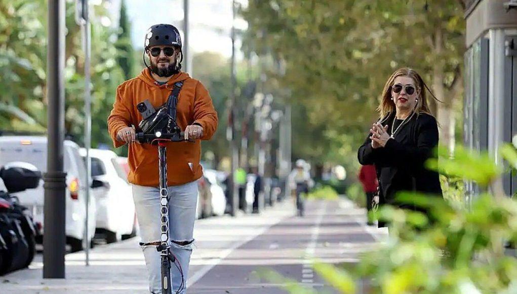 Usuario de patinete eléctrico circulando por una vía urbana habilitada, con casco y respetando el espacio de los peatones.